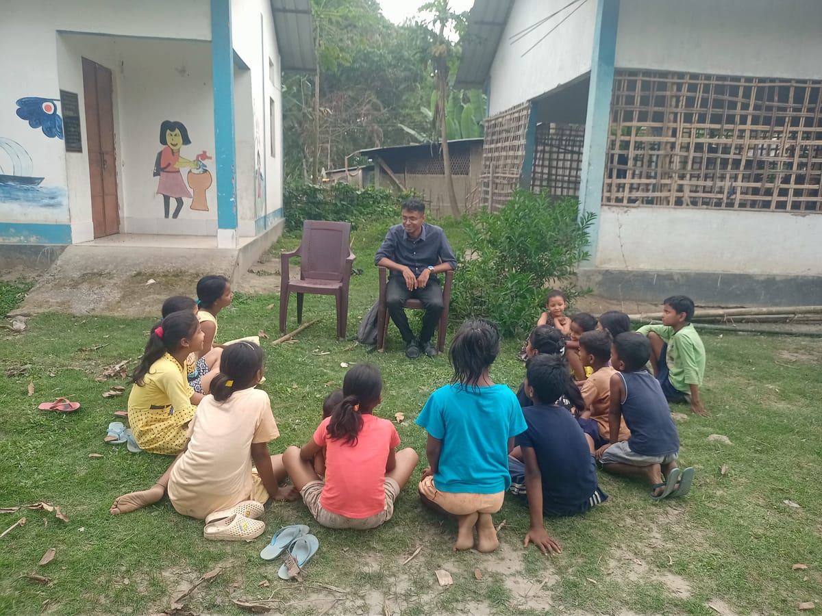 An NPoC fellow sitting with a group of children outside a village school