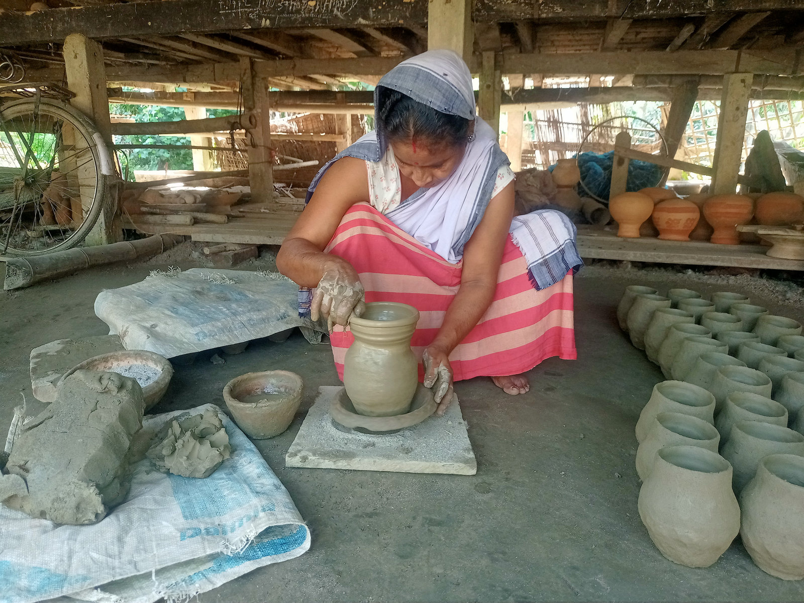 A woman shapes clay pots in a workshop in Majuli
