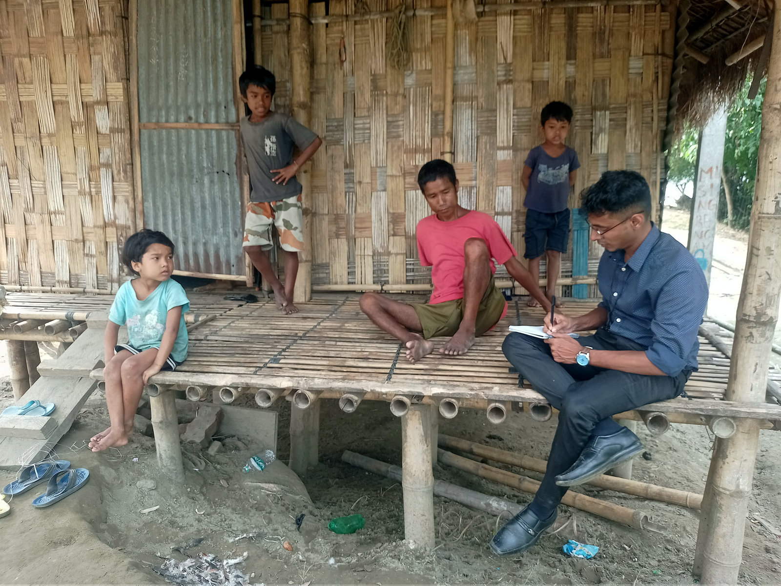 An NPoC researcher interviews a family on the porch of their bamboo house